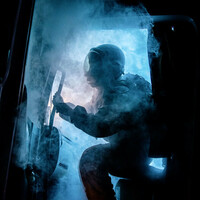 The cabin door of a truck opens, spewing eerie blue smoke. Silhouetted by a bright blue light that cuts through the darkness of night, a figure wearing an astronaut uniform begins to emerge.