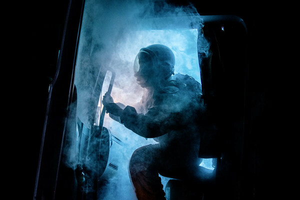 The cabin door of a truck opens, spewing eerie blue smoke. Silhouetted by a bright blue light that cuts through the darkness of night, a figure wearing an astronaut uniform begins to emerge.