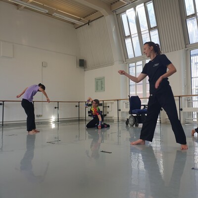 4 people in a dance studio, they are moving around being instructed by a dance teacher.