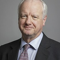 This is the official portrait of Lord Russell of Liverpool. Lord Russell has grey hair and is wearing a dark suit with a lighter shirt and patterned tie.