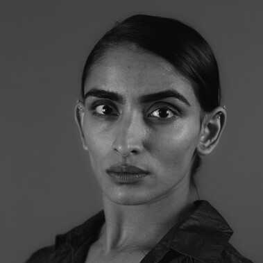 Headshot of a woman looking at camera with her hair tied back in a grey top, image is in black and white