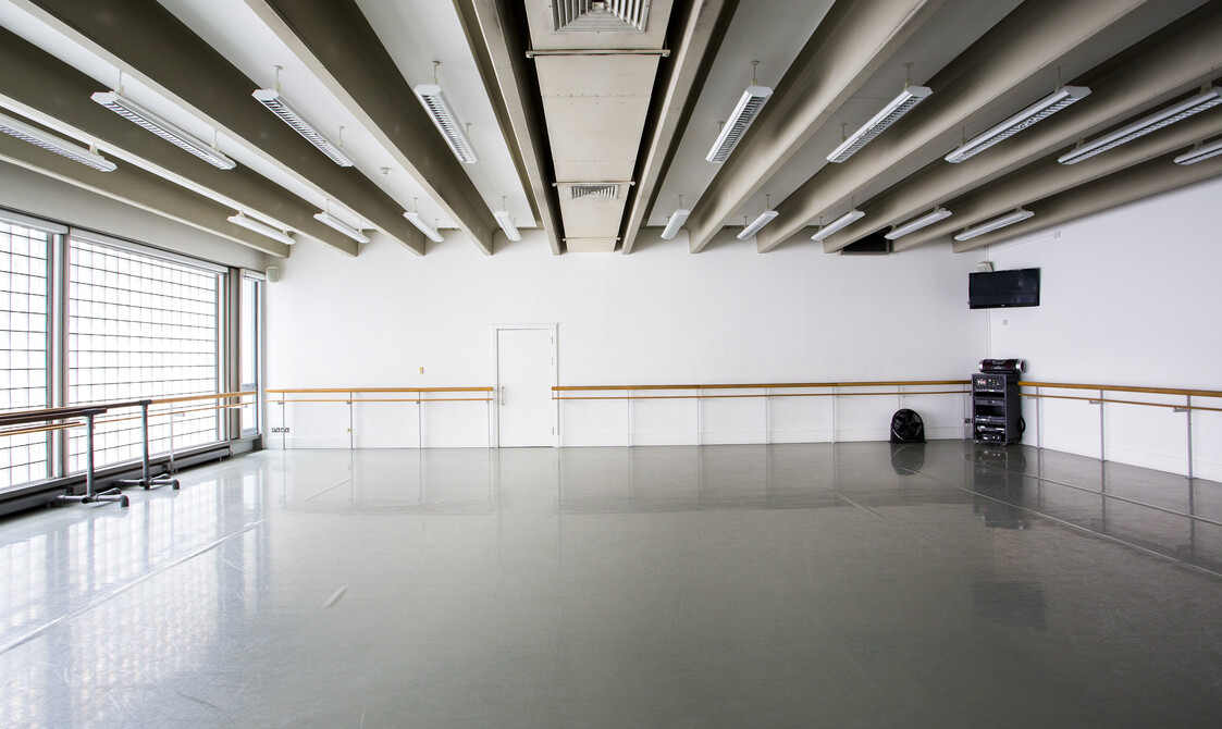 Image of an empty studio with ballet bar on the far wall, windows on the left