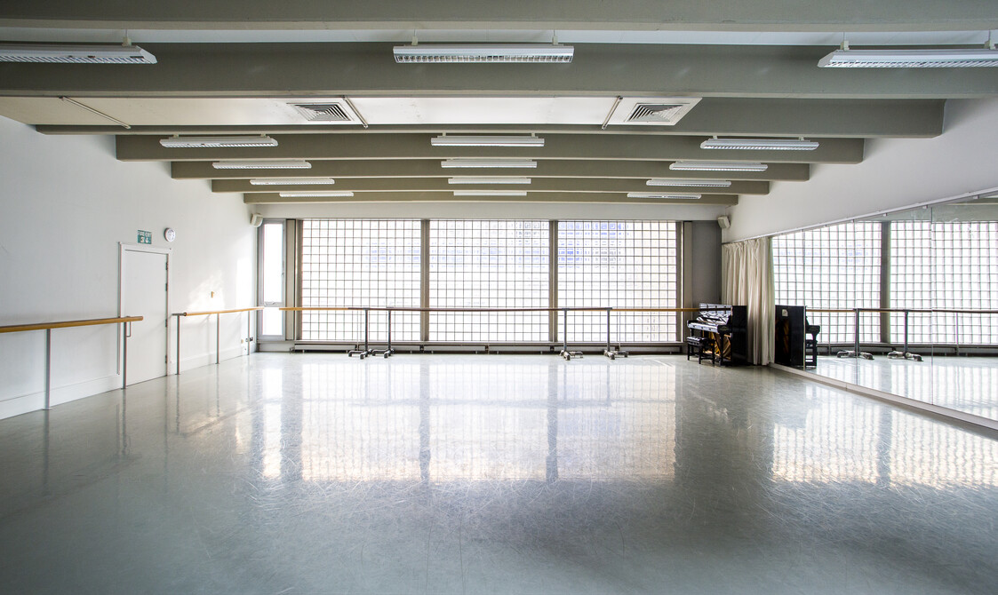 image of an empty studio with mirrors on the right hand side, windows on the far walls with ballet barres across the windows and along the left wall