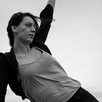 Black and white image of Adrienne Hart, wearing a lighter top and darker cardigan. She gazes into the distance.