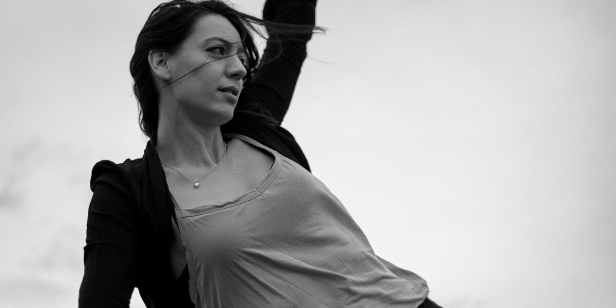 Black and white image of Adrienne Hart, wearing a lighter top and darker cardigan. She gazes into the distance.