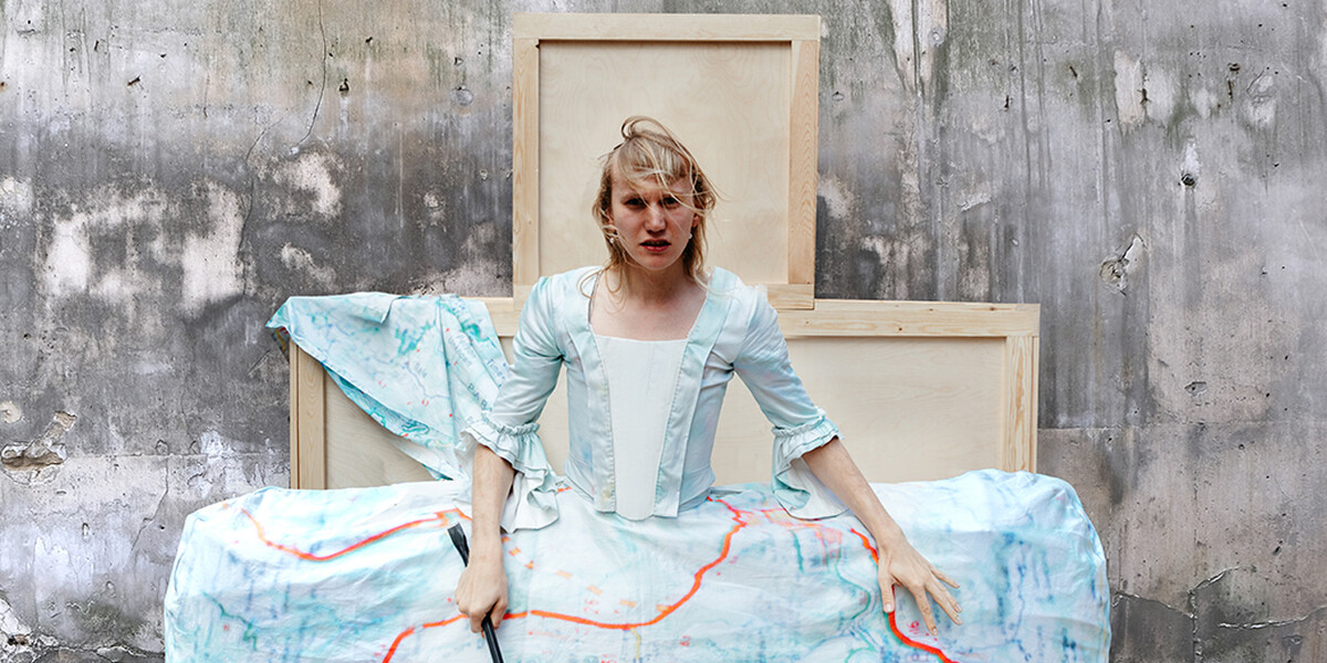 Anders Duckworth stands in a costume that resembles a 15th century dress with a greatly exaggerated skirt made out of a map.