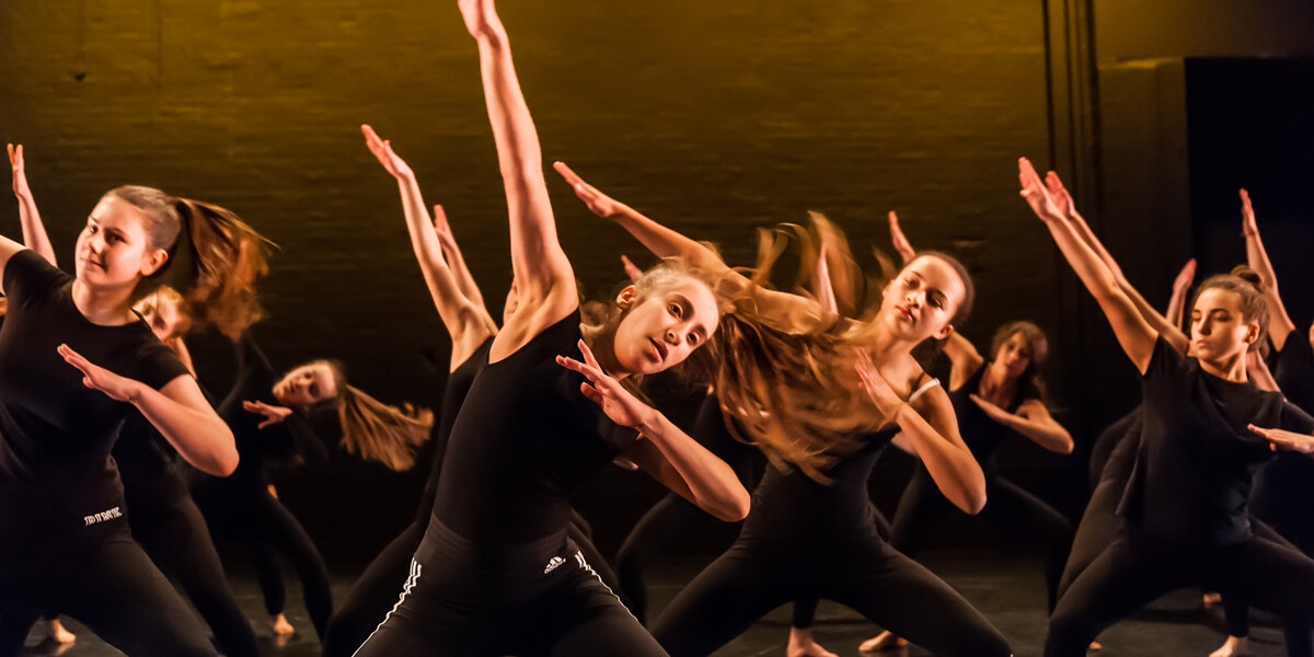 A group of secondary school students on The Place stage wearing black tops and trousers dancing
