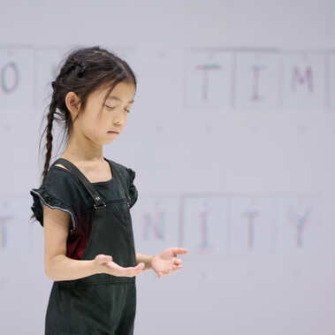 A photo of a child performer with eyes closed and hands outstretched in front of them.