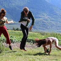 Image of three dancers dancing on green grass in the foreground. In the background are mountains