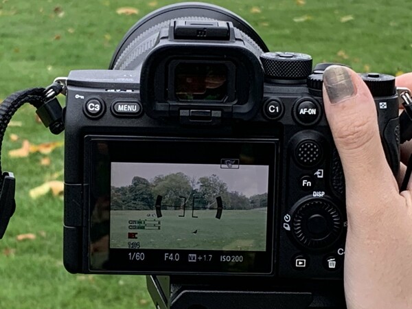 A camera with three people in shot, they are stood in a park