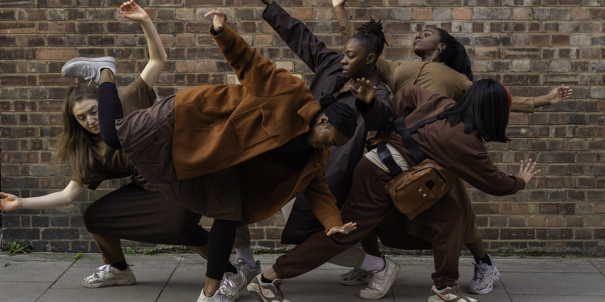 Image of five dancers all in a group huddled together. They make different shapes with their arms and bodies.