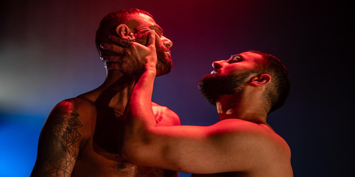 Two men embrace in atmospheric pink and blue lights