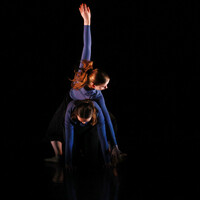 An image of two dancers from Thrive Youth Dance Company creating a shape together, one of them in all fours position and another connected through their back and reaching up with their arm.