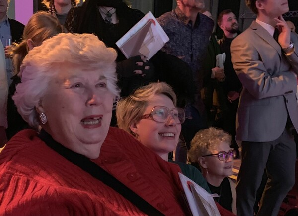 A group of people appear to be watching something in the distance, there are two woman are smiling, one is older and the other is younger