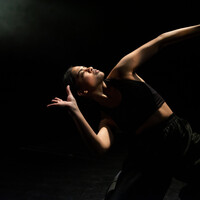 Image of a dancer. The background is black and they are arching over to the right hand side.
