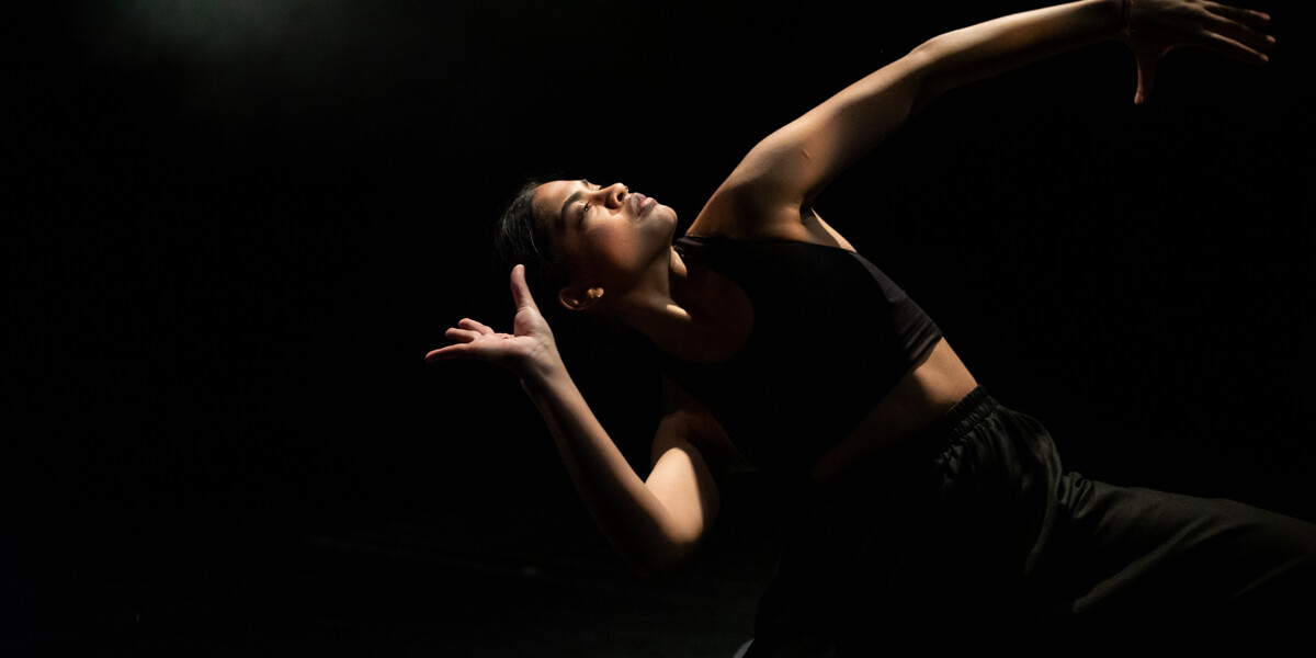 Image of a dancer. The background is black and they are arching over to the right hand side.