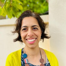 Image of Shaparak Rahimi. Shaparak has dark hair and is wearing a yellow cardigan and a blue top. She is smiling.