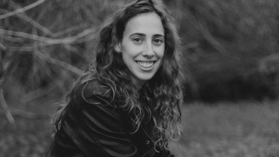 Black and white photo of Sivan in nature. She is looking at the camera smiling. She has long curly hair.
