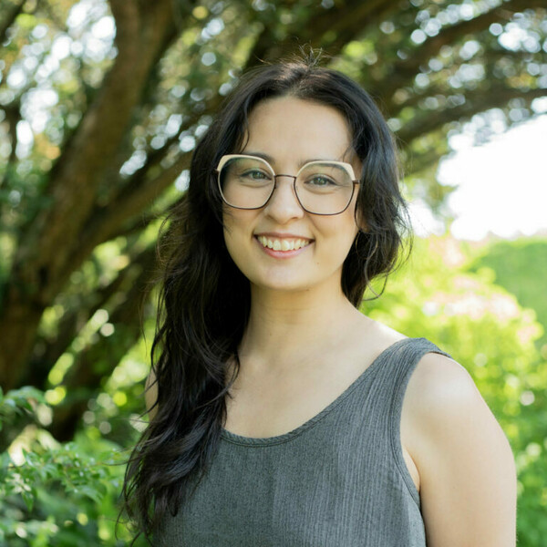 Sophia's headshot against a leafy green backdrop on a sunny day