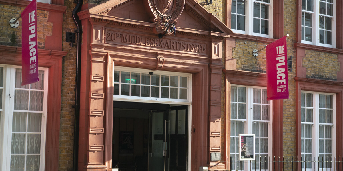 The Place Building entrance close up on a sunny day with pink branded flags