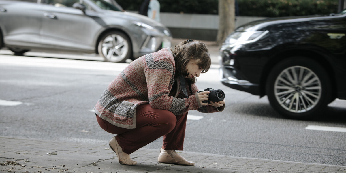 Student with a camera, kneeled down on the street to capture a shot