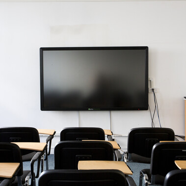 A lecture room is set up with individual chairs with desks facing a screen.