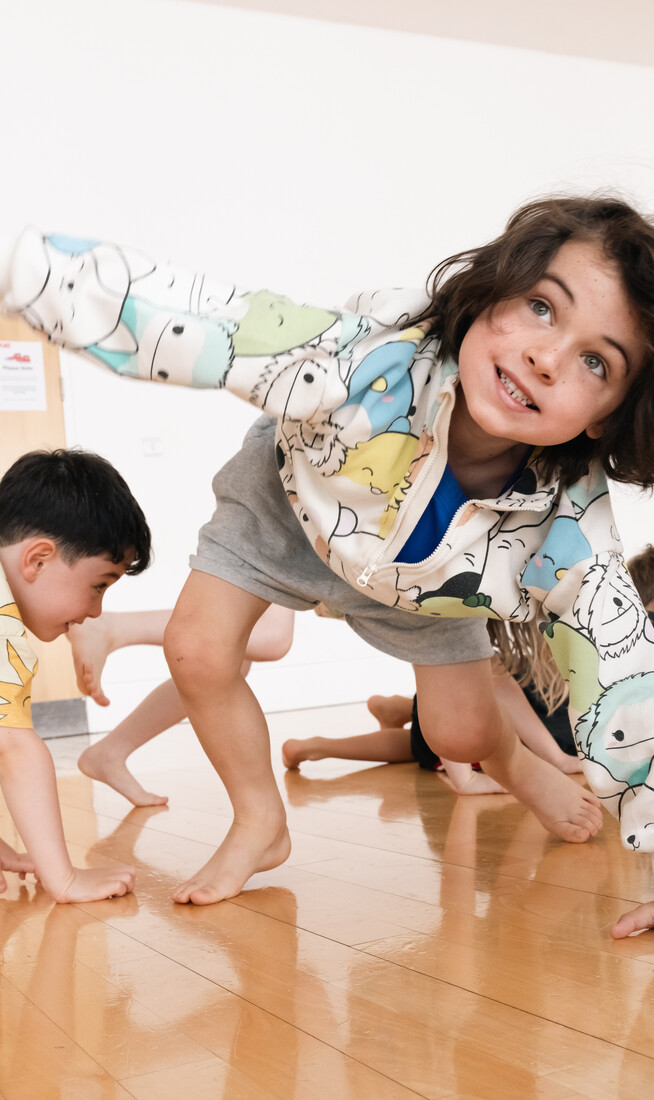 A group of kids aged 3-5 wearing casual clothes moving across a dance studio floor with their hands and feet.