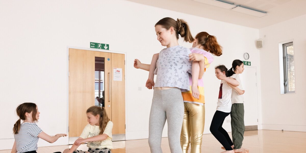 Two girls aged 10 standing back to back with their arms linked in a dance class.