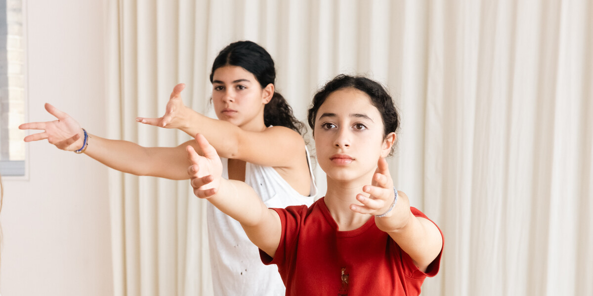 Two girls, one in a red top and the other in a white top, lunging forwards with arms outstretched.
