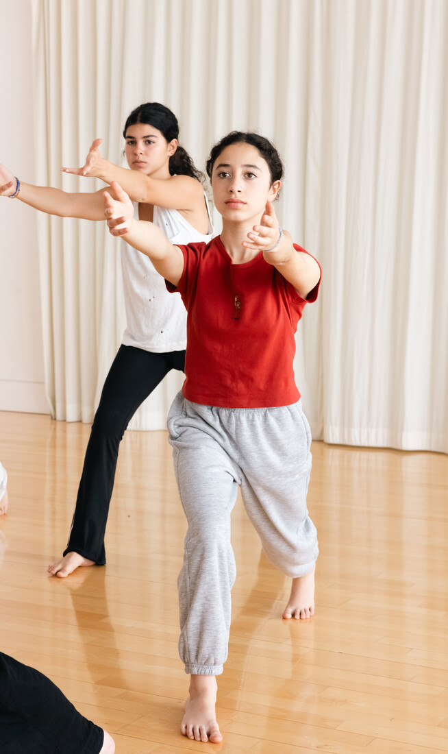 Two girls, one in a red top and the other in a white top, lunging forwards with arms outstretched.