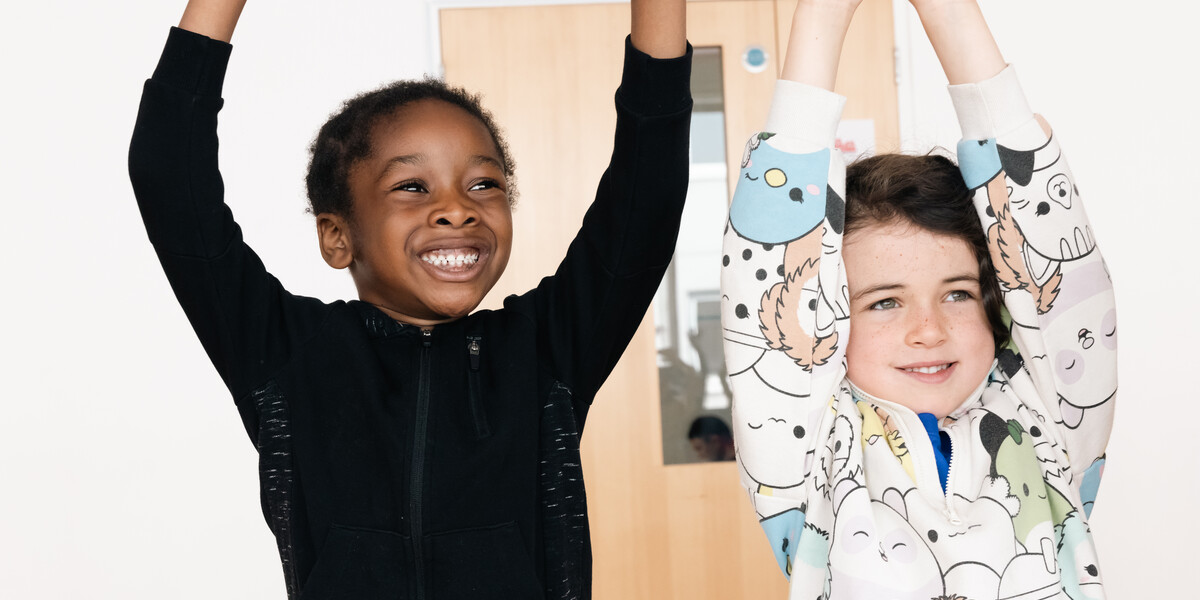Two boys with their arms up in a dance studio.