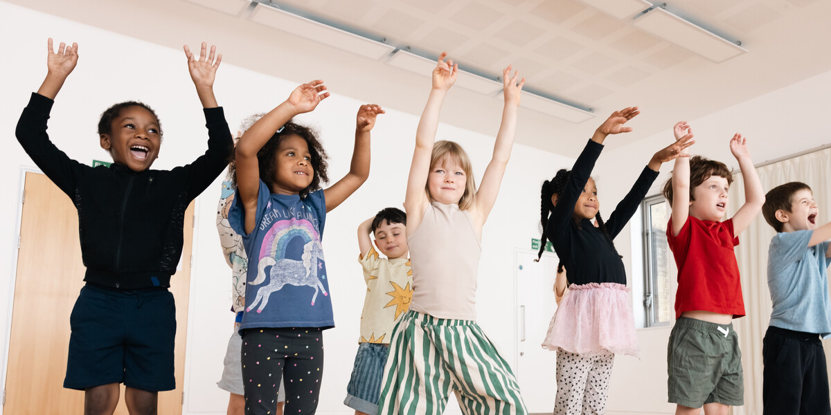 Children smiling and dancing with their arms above their head.