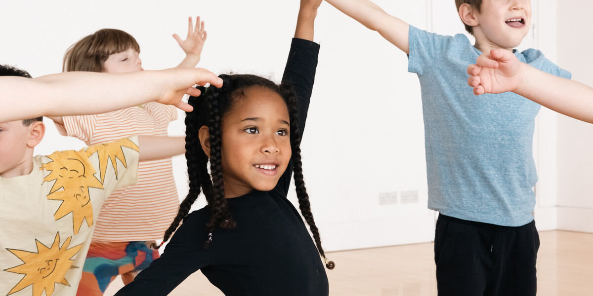 A girl around 5 years old dancing with her arms stretched out, wearing a black top and pink tutu.