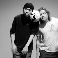 Image of two dancers. They hold a football between their heads. One dancer is wearing black and has a black hat on. The other is wearing a white graphic t-shirt.