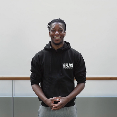 Person standing in a dance studio wearing a black hoody with The Place logo printed on it